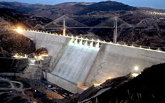 Night-time aerial view of the central part of the dam, with a suspension bridge at the bottom of the dam