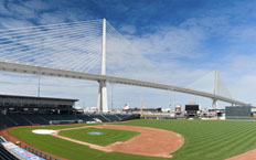 Vista frontal de una sección del puente, se puede apreciar un campo de beisbol en primer plano con el puente al fondo